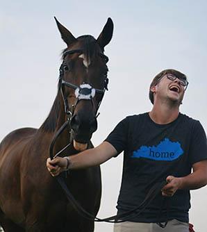 Zachary Chaney laughing as a horse sticks out its tongue.