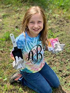 A little girl proudly displays her gardening tools.