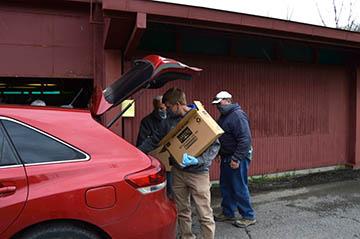 Three men loading food boxes in the back of a red car. Three men loading food boxes in the back of a red car.