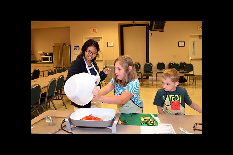 Kendra Oo, left, helps Marley McKoy and Jacob Miles with their stir fry recipe during Boyd County's Kids Can Cook. 