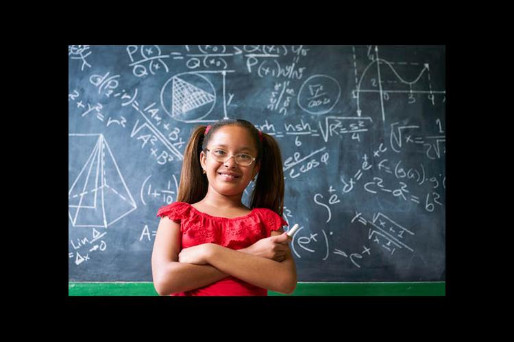 A girl stands in front of a blackboard filled with math equations. 