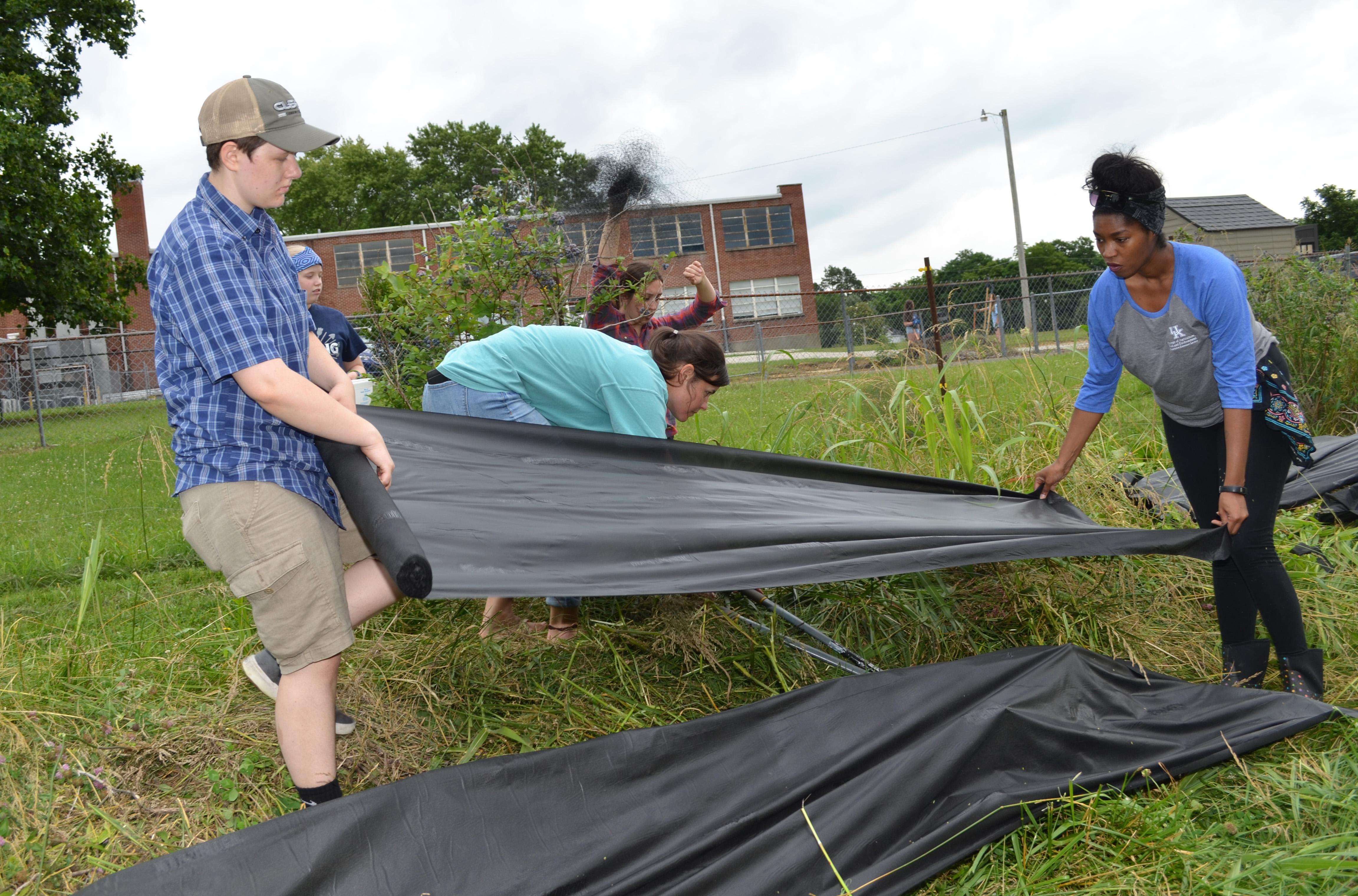 Garden volunteer Grace Lowe, left,  and LaToya Drake, Barren County family and consumer sciences extension agent, place black cloth over the swales to help with weed control. Photo by Katie Pratt, UK agricultural communications.