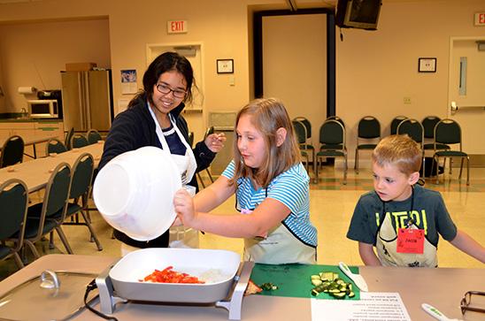 Kendra Oo, left, helps Marley McKoy and Jacob Miles with their stir fry recipe during Boyd County's Kids Can Cook. 
