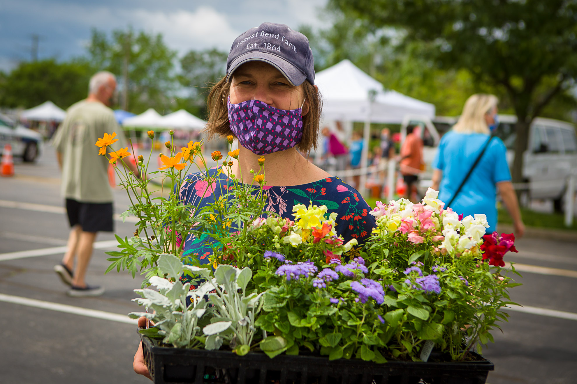 A vendor at the Lexington Farmers Market shows off some of the plants she has for sale, while wearing a mask to protect customers during the COVID-19 pandemic. Photo by Matt Barton