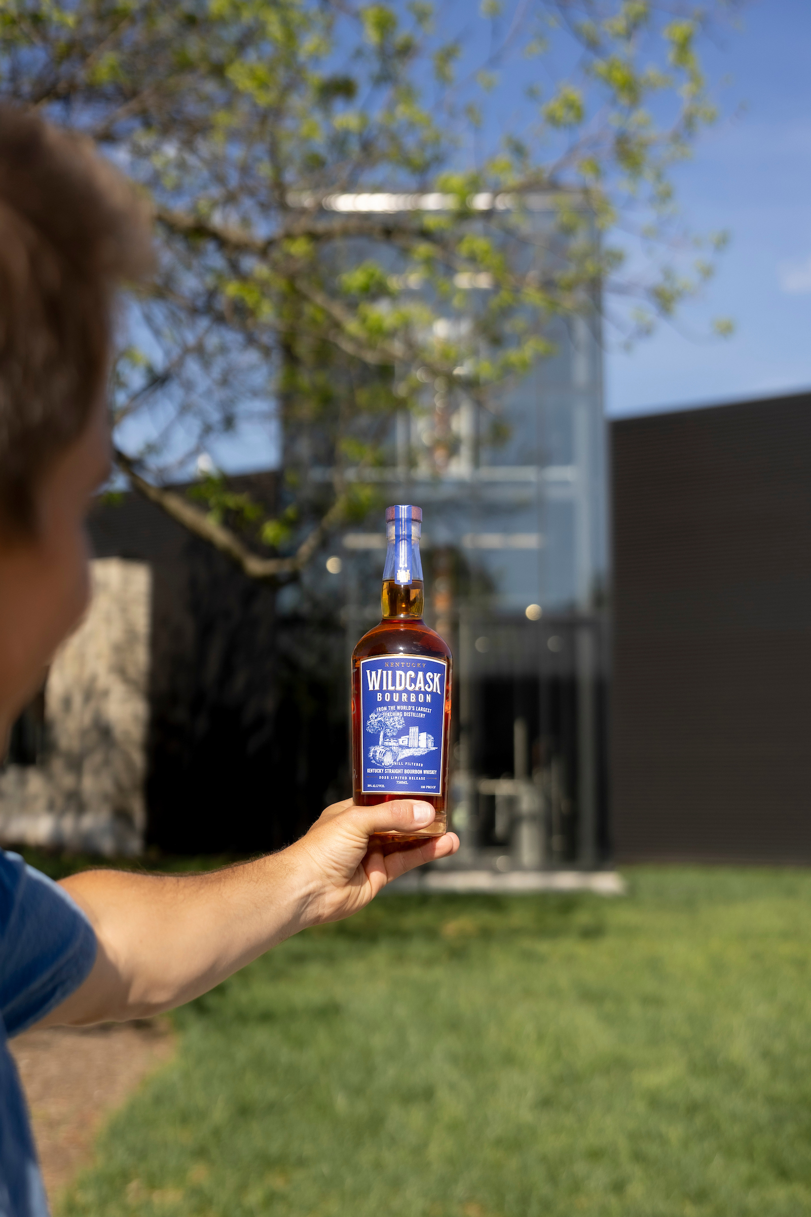 Set DeBolt holding up WildCask bottle in front of JBBI building