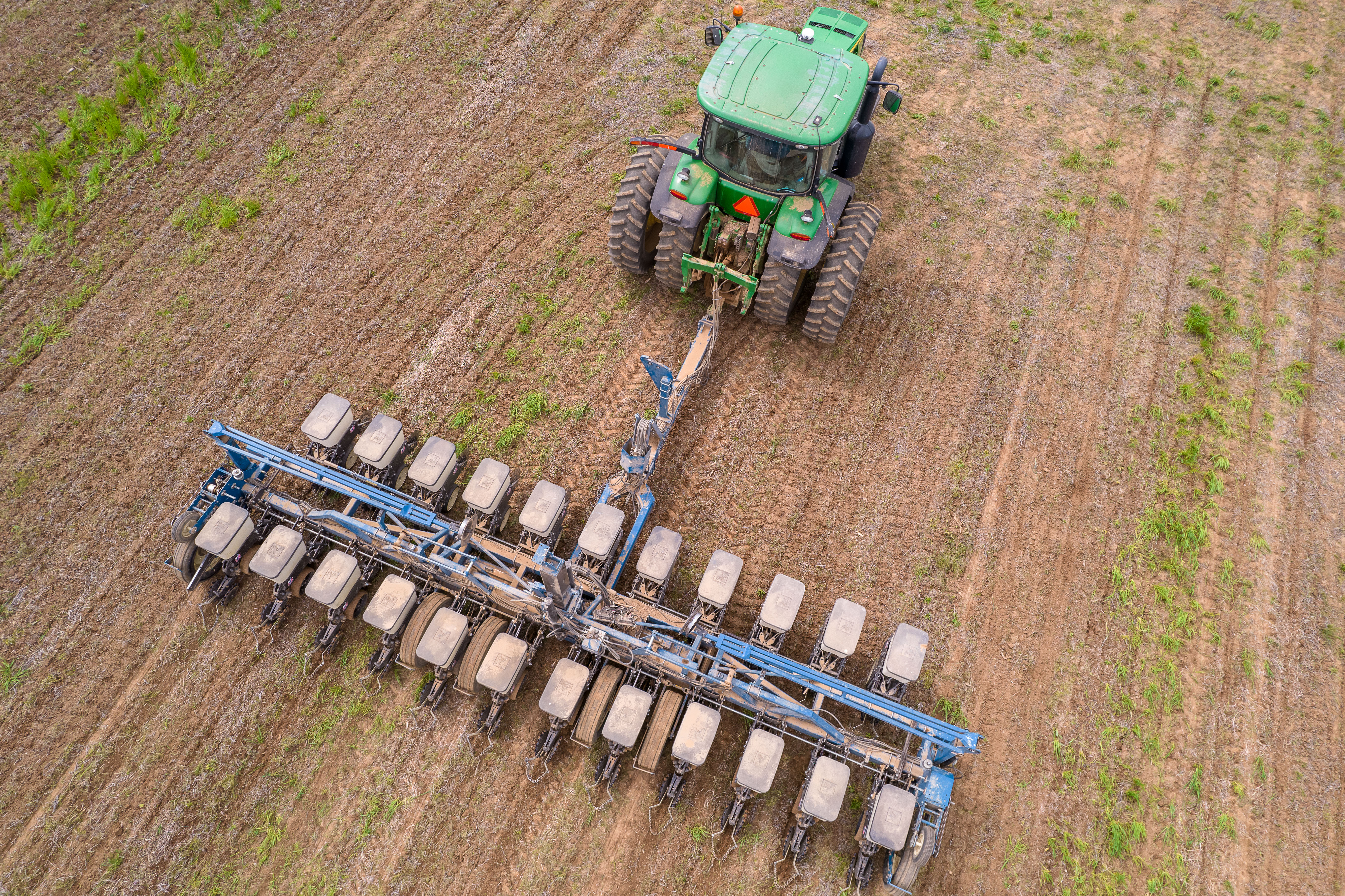 An aerial shot shows a tractor pulling a no-till seeder through a field. 