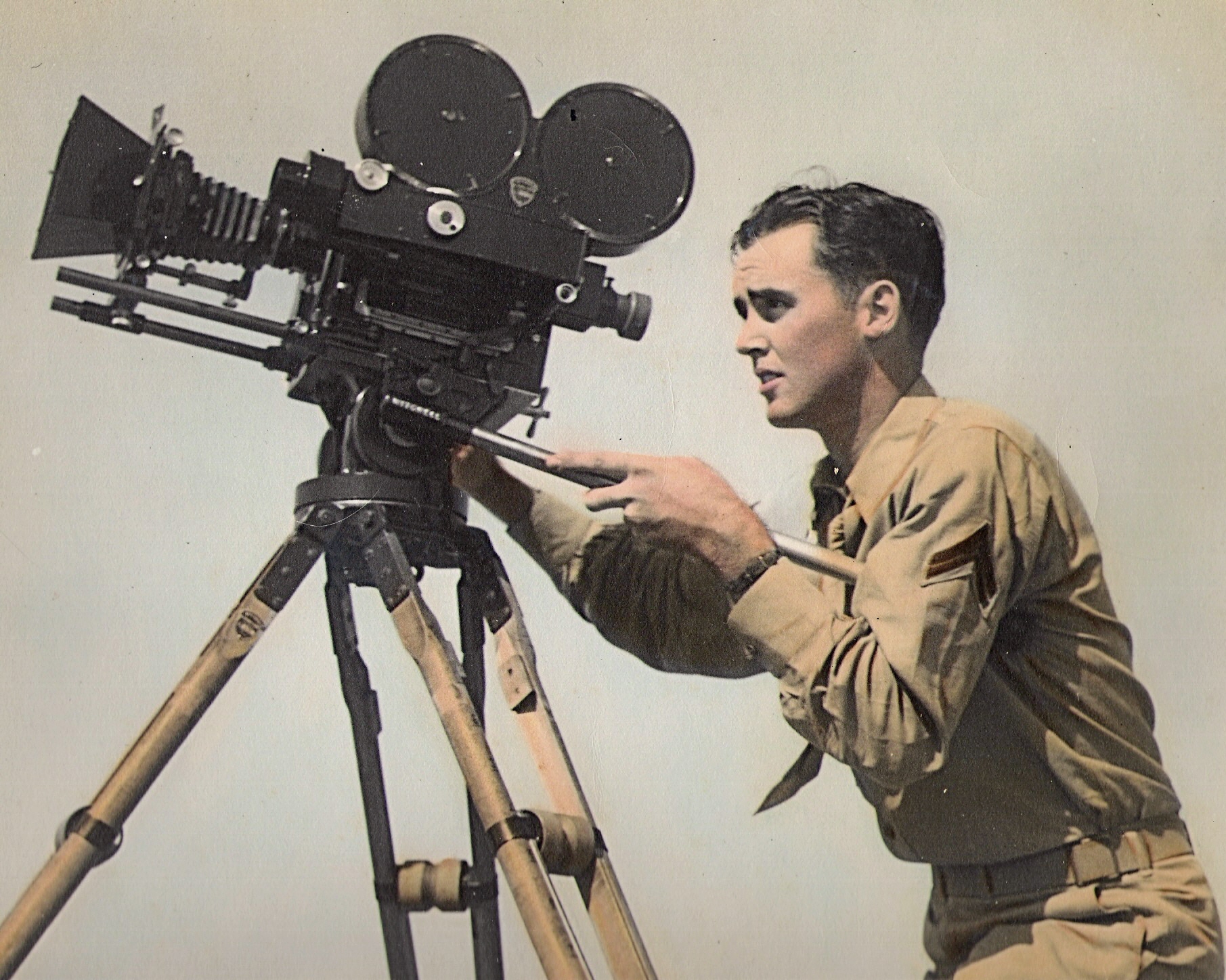 A young man in military dress operates a vintage video camera. 