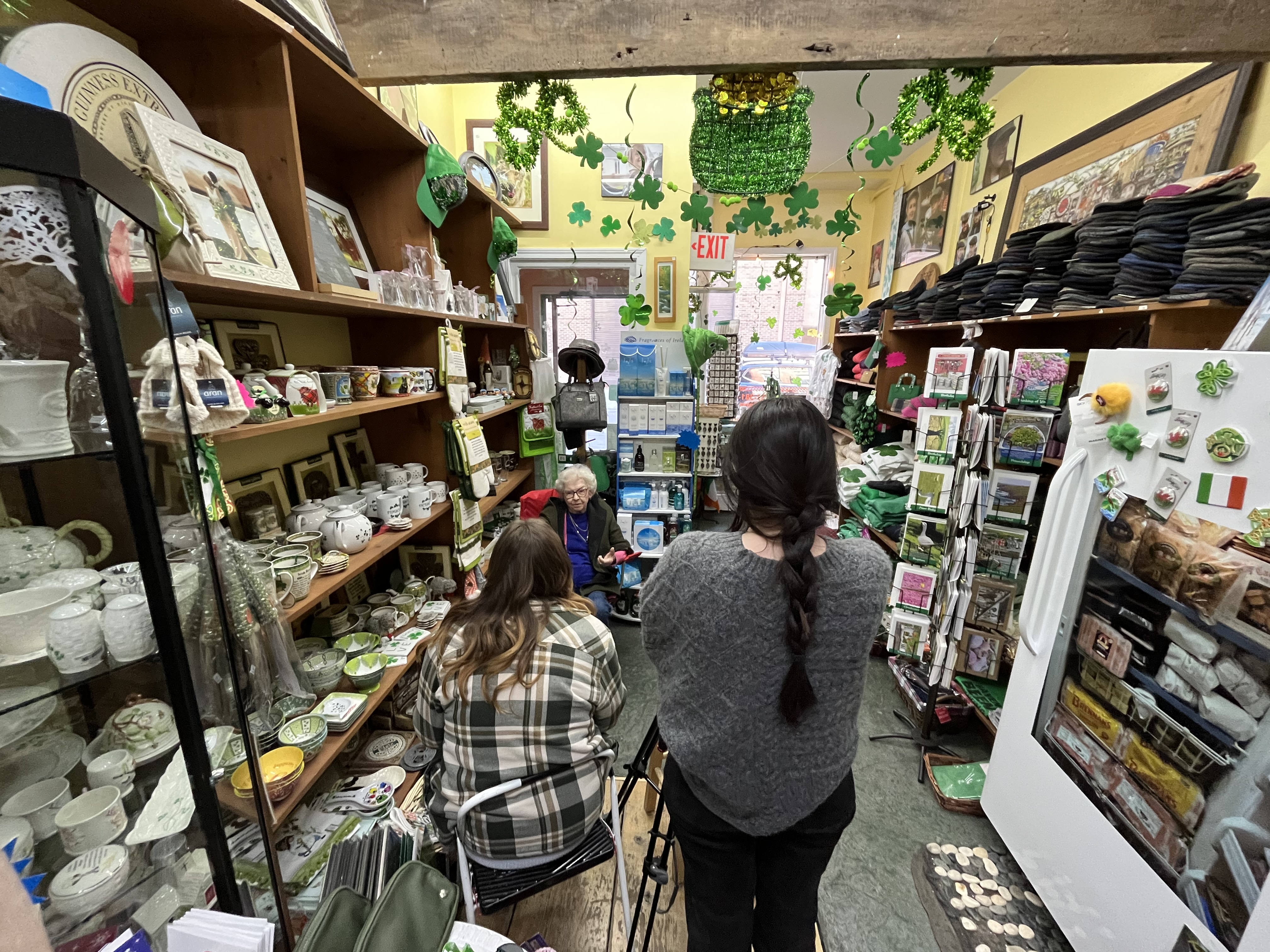 Two college students use cameras to record an interview with a woman sitting in an Irish good shop.