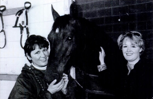 In a black-and-white photo, two women pose with a horse.