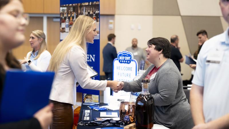 Student shaking hands with employer over table at career fair.