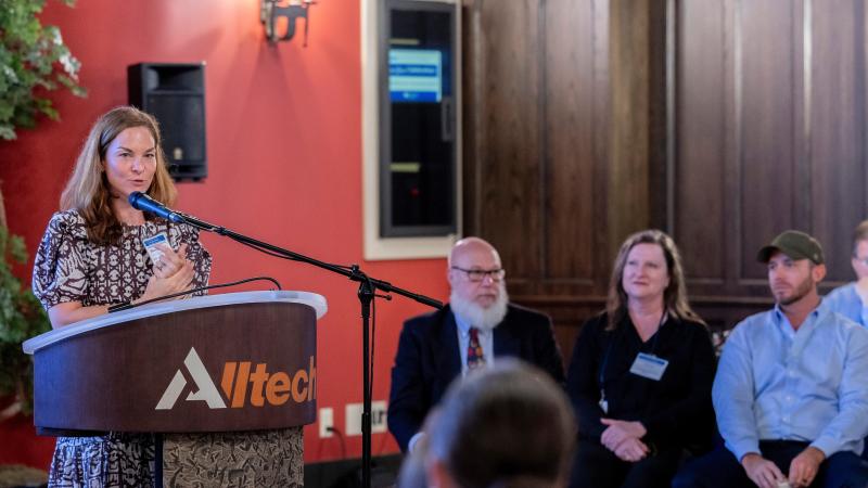 Alison Gustafson giving remarks at an Alltech podium with a red wall behind her.