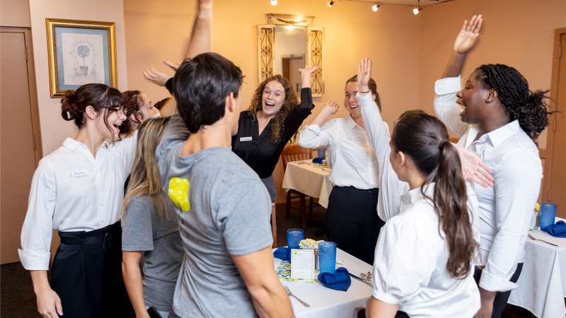 Eight students raise their hands in the air after a "go, team" cheer.