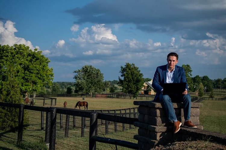 Nick D’Amore uses laptop while perched on a wall at UK Maine Chance Farm