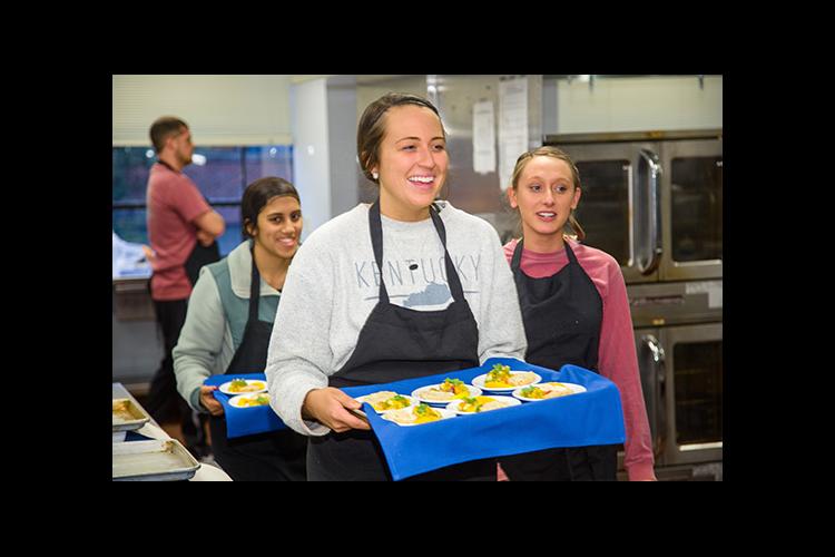 Taylor Runyon, center carries out recipes for taste test panelists at UK. UK students Monica Shah and Hannah Mayse follow. 