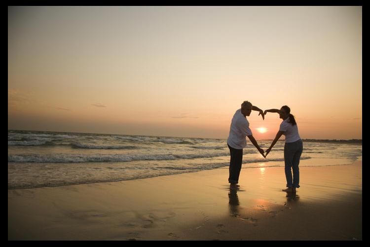 Sunset beach scene of couple making heart shape with arms
