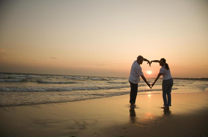 Sunset beach scene of couple making heart shape with arms