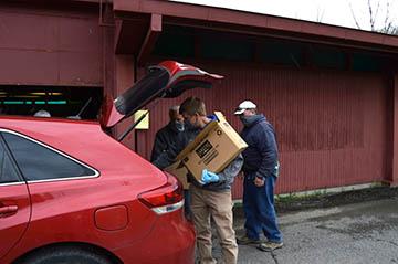 Three men loading food boxes in the back of a red car.